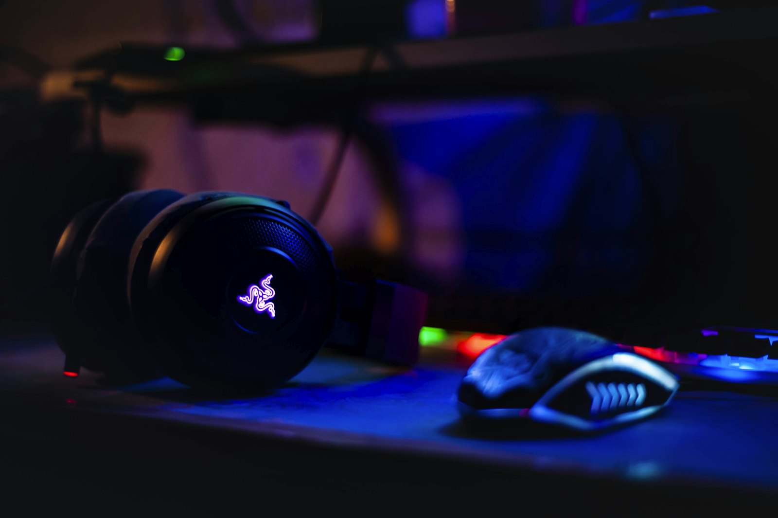 Gaming headset with backlit earcups on a desk beside a mouse and keyboard