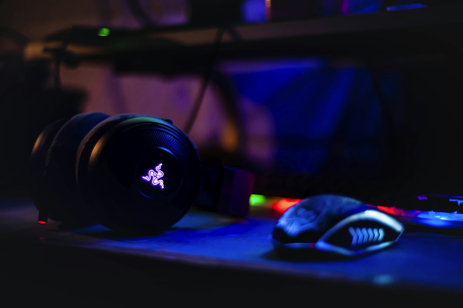 Gaming headset with backlit earcups on a desk beside a mouse and keyboard